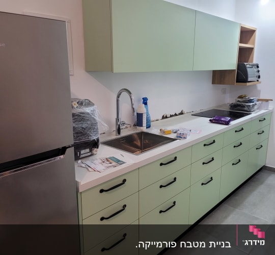 מטבח עם מקרר, כיור, ארונות ירוקים ותנור